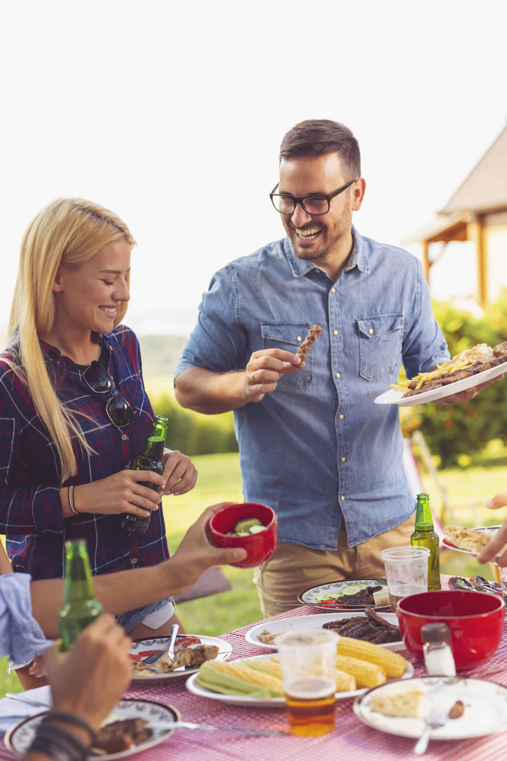 Group of friends having an outdoor barbecue lunch, eating grilled meat, drinking beer and having fun